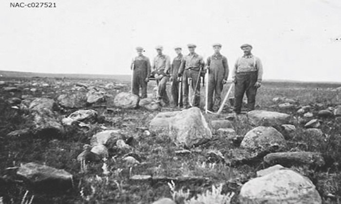 A train is stopped in a small town next to a train station and two elevators.