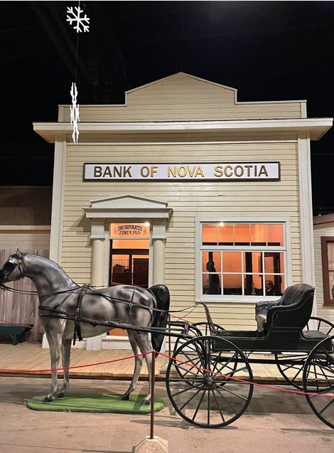 A group of men are working together to build a wooden grain elevator with piles of lumber nearby and a train in the background.