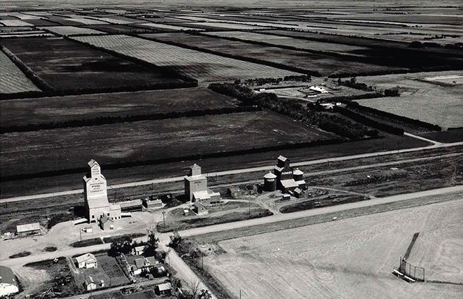 A train is stopped in a small town next to a train station and two elevators.