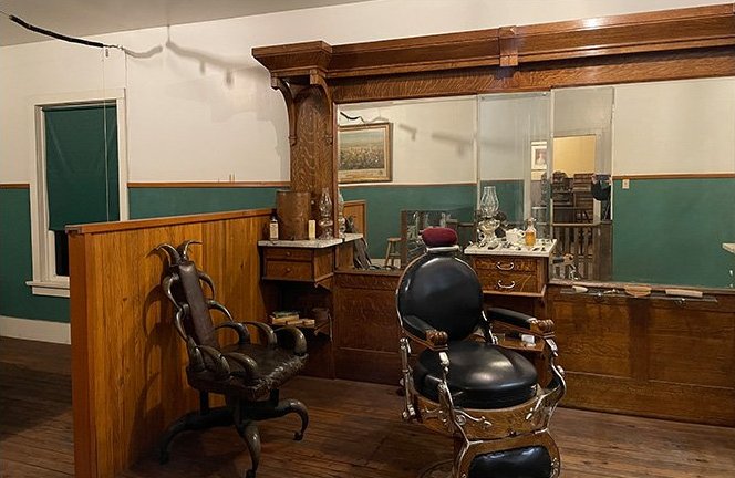 A mother and her three children are sitting down by their car to have supper in the field during harvest time.