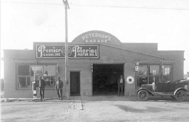 A mother and her three children are sitting down by their car to have supper in the field during harvest time.