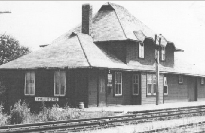A train is stopped in a small town next to a train station and two elevators.