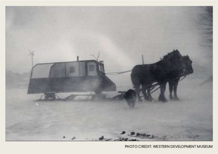 Two horses are hooked up to a homemade sled that is used as a shelter from the cold when traveling in the winter. There is a roof on the sled to protect people from bad weather conditions.