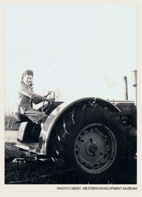 A farm wife smiling as she drives a tractor.