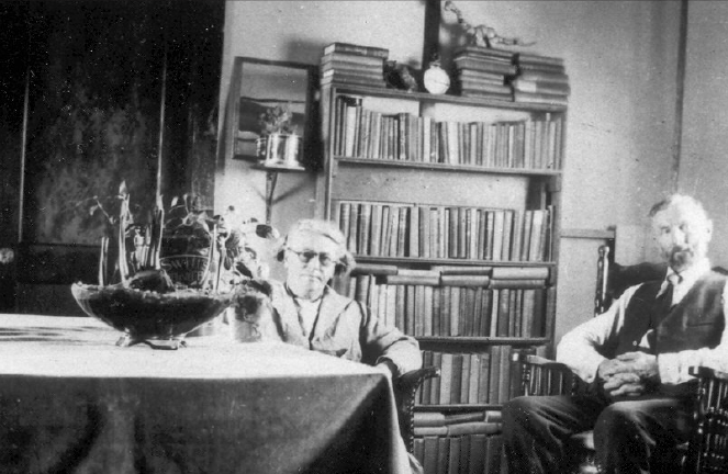 A mother and her three children are sitting down by their car to have supper in the field during harvest time.