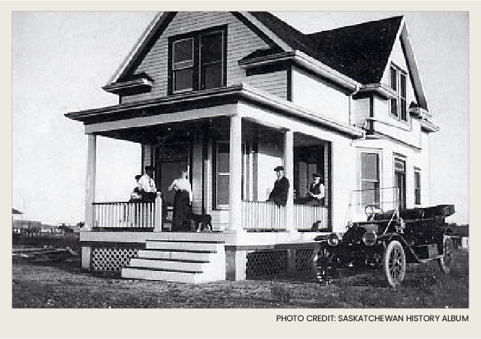 The outside of the house has a car parked next to it and a group of people sitting on the front porch.