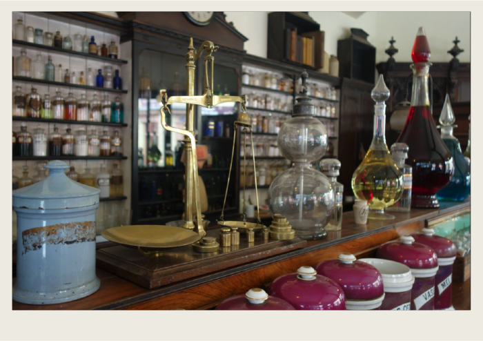 The inside of a pharmacy is shown with shelves full of jugs and glass jars that have medicines in them. 