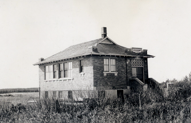 A mother and her three children are sitting down by their car to have supper in the field during harvest time.