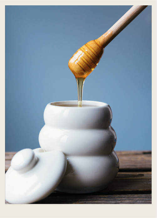 Photo caps-02 A jar of honey with a spoon dipping into it.