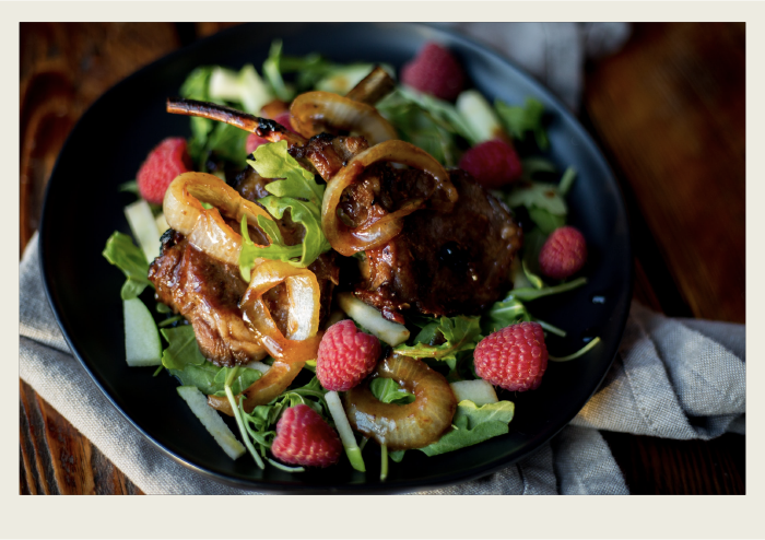 A lamb chop on top of a salad is shown. 