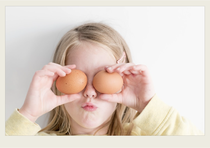 Photo caps-03 A girl is holding an egg in front of each eye.