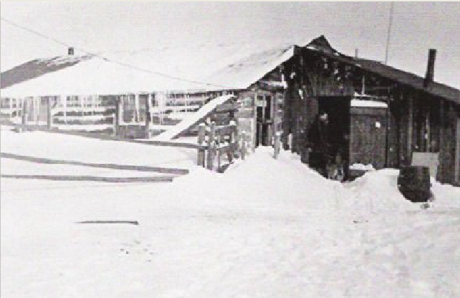 A log house in winter is covered in snow and ice, showing that the weather has been cold and blizzarding.