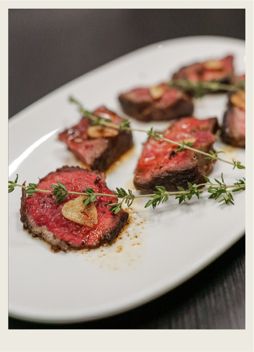 A rare steak sits on a plate with herbs and butter.