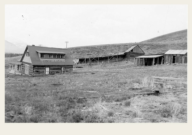 Past-Ranching-Ranching-History A ranch with a house and barn and fences stand in the bottom of a green-grass valley.