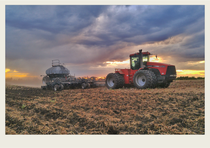 Photo caps-01 A red tractor is pulling an air seeder in a field with a sunset in the background.