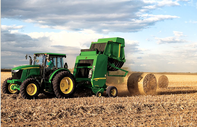 A green tractor is pulling a baler that is completing and kicking a bale out into the field.