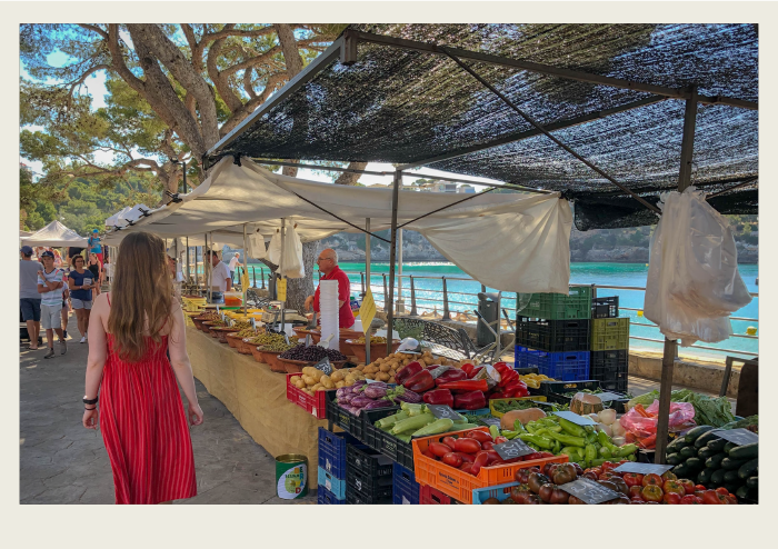 A woman walks through a farmers’ market, looking at different stalls of fruit and vegetables.