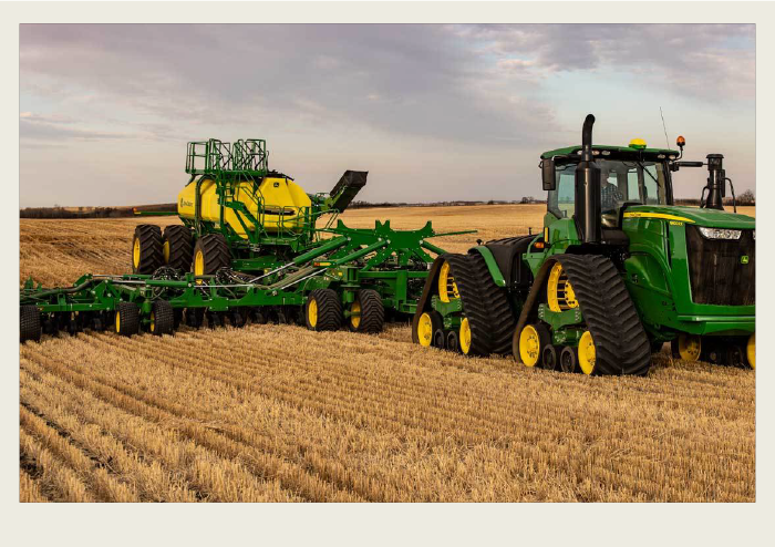 Photo caps-07 A modern green tractor with triangular-shaped tires pulls an air drill seeder to seed a field.
