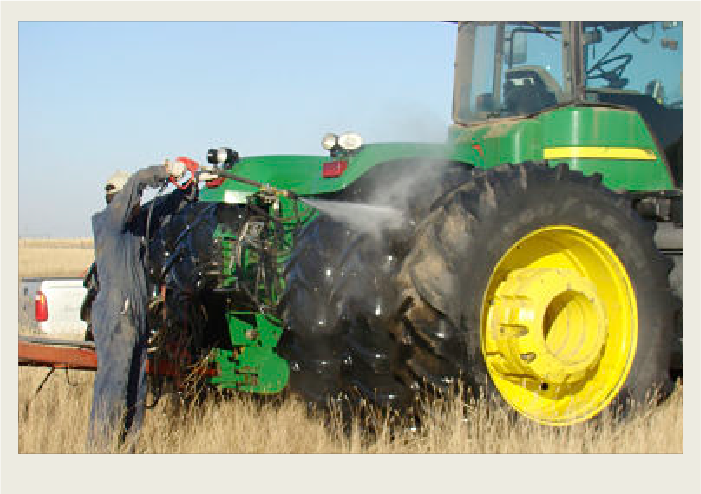 Photo caps-08 A farmer wearing overalls is rinsing the tractor’s tires with water and a spray hose in the field.