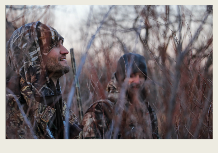 Photo caps-10 Two hunters wear camouflage clothing stand in tall grass so it is hard for animals to see them.