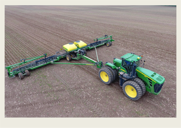 A green tractor pulls an air seeder to seed the large field.