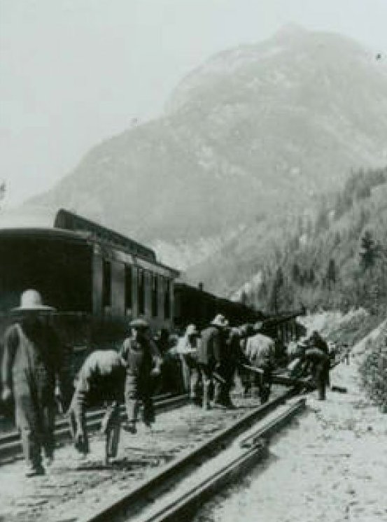 A group of Chinese men are working on the railway with mountains and a train in the background.