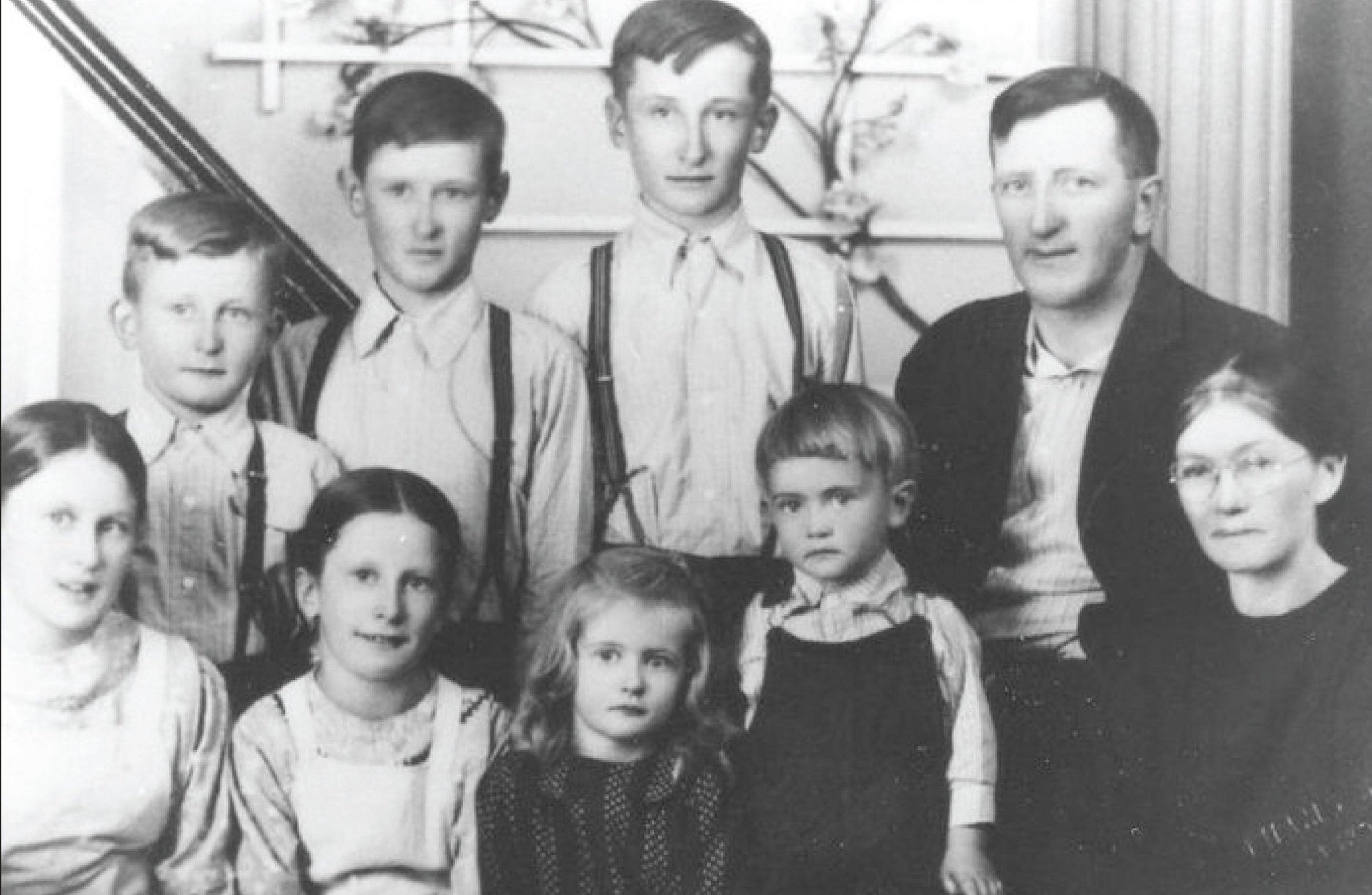 A Mennonite couple and their seven children pose for a photo. The boys wear their hair short and combed to the side, and the girls wear their hair long and pulled back.
