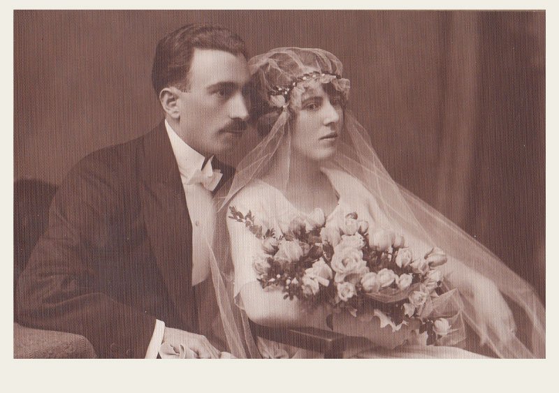 A Romanian man and woman are posing for a photo on their wedding day dressed in a suit and wedding dress, respectfully.