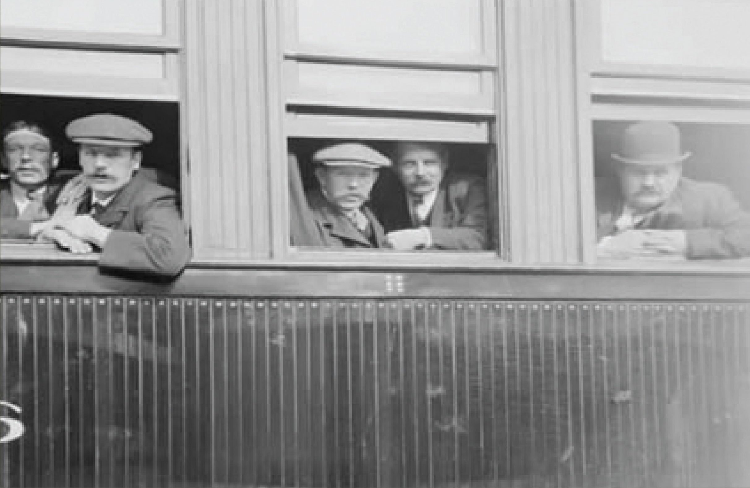Five Scottish men stare out 3 separate windows from the inside of a train before they depart out West.