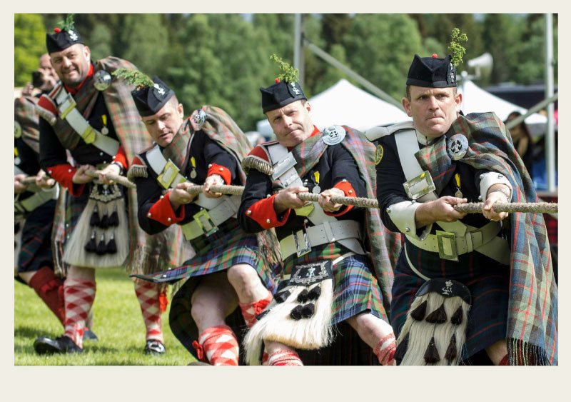 A line of men are dressed up in traditional Scottish outfits and pulling together on a rope in a tug-o-war event, as part of Highland games.
