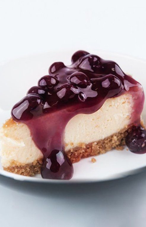 A slice of cheesecake is on a plate with Saskatoon berries on top.