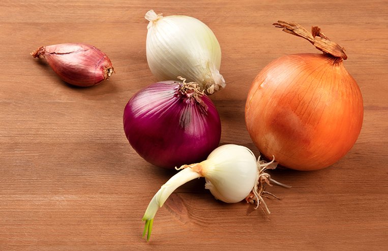Five different varieties of onion sit on a table.