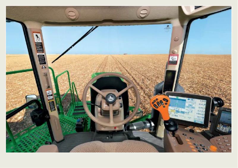 The inside of a tractor is shown including the steering wheel, controls, and a monitor with GPS on it.
