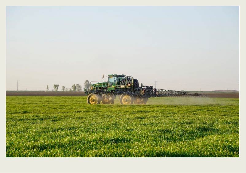 Mist comes out of a high clearance sprayer as it drives across a green field.