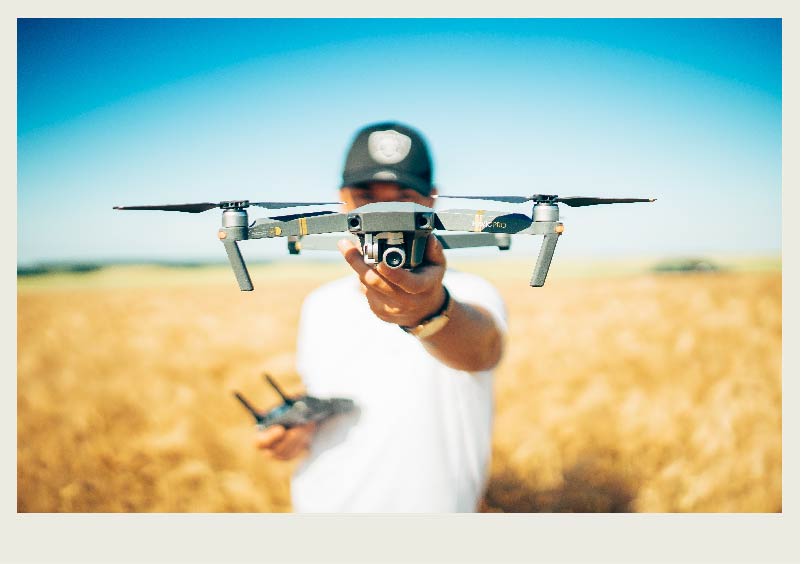 A person stands in wheat field holding a drone close to the camera.