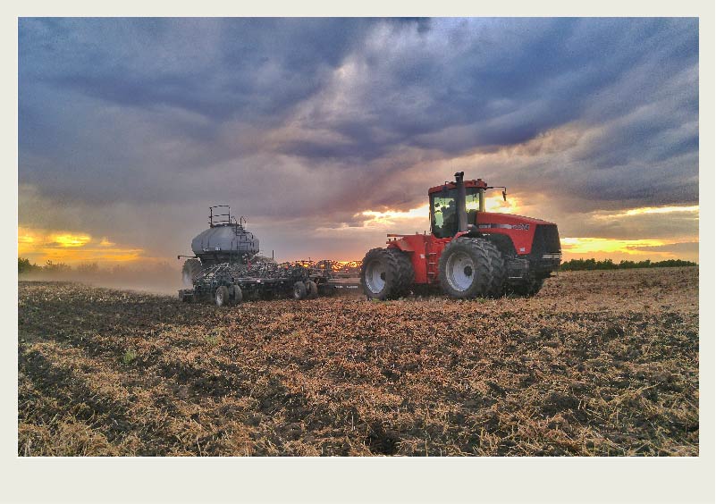 A tractor pulls an air seeder in a field with a sunset in the background.