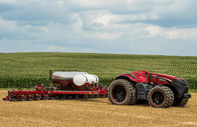 A red tractor with no cab for a driver pulls a piece of equipment in a farm field.