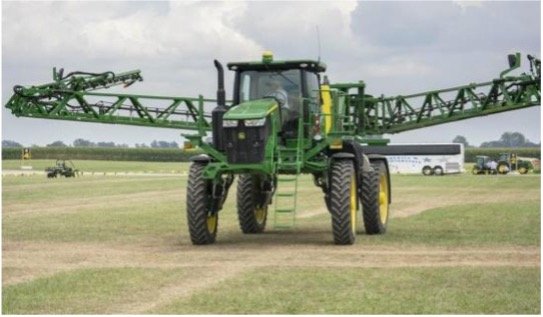 A high-clearance sprayer is in a green field with its booms out.