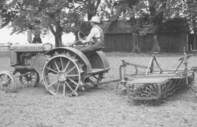 A farmer rides on a tractor pulling equipment in a farm field