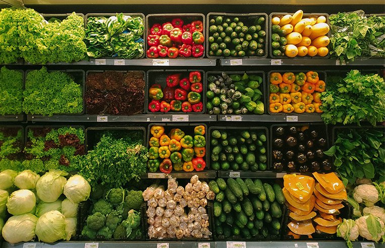 Evolution-Trade-NationalTrade-SellingProducts This vegetable isle at the grocery store has a variety of vegetables including peppers, cucumbers, cabbage, broccoli, lettuce, and herbs.