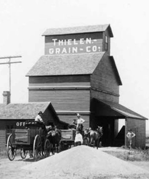 A farmer pulls a grain cart full of wheat up to an elevator.