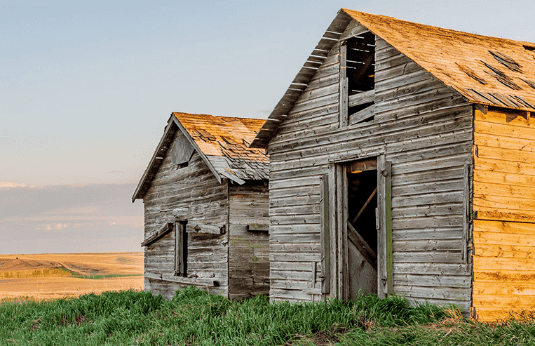Two wooden grain bins are shown together in a farm field.