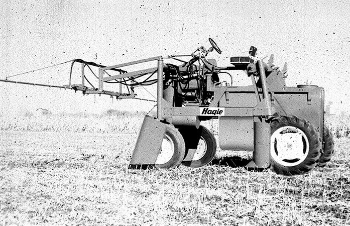A high-clearance sprayer is shown in a farm field with one front-mounted boom.
