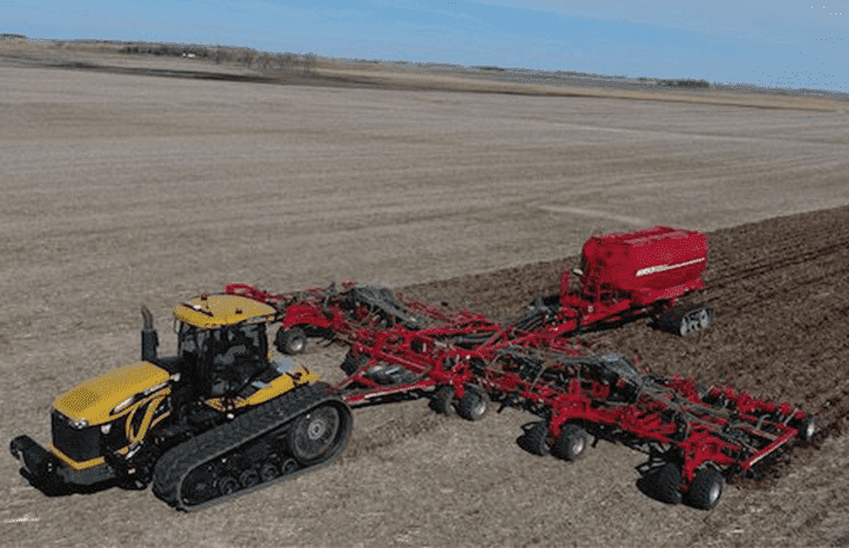 An aerial view of a farm field shows a tractor pulling an air seeder.