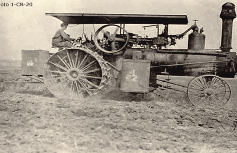 A man is steering a tractor with steel wheels in a farm field.
