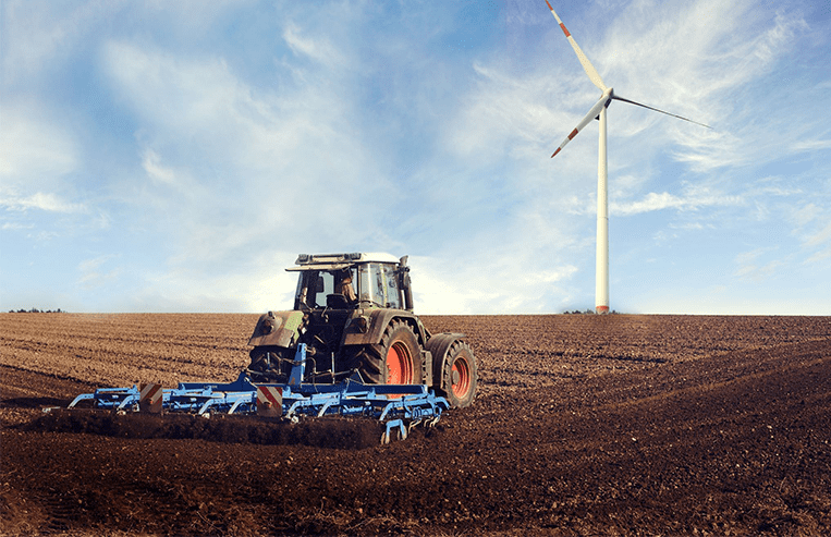 A tractor pulls a cultivator through a bare farm field.