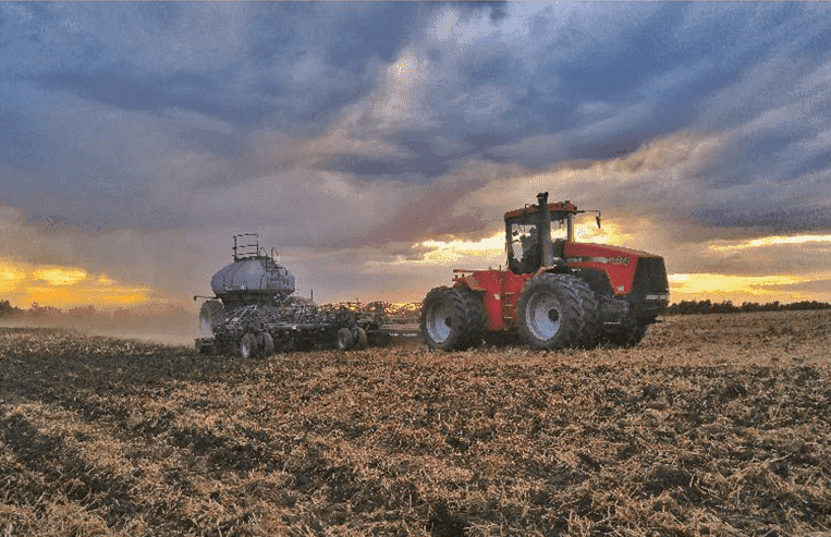 A man is steering a tractor with steel wheels in a farm field.