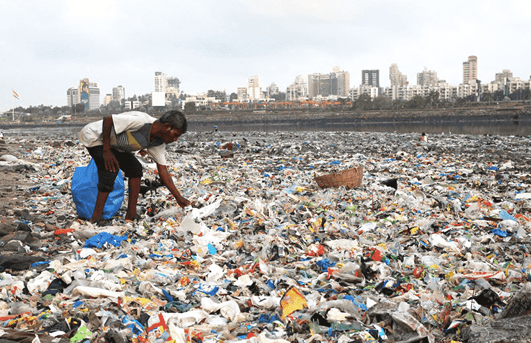 Evolution-FutureofFarming-FutureofByproducts-Bioplastics1 A person cleans up thousands of pieces of litter in an open area that has a city skyline in the background.