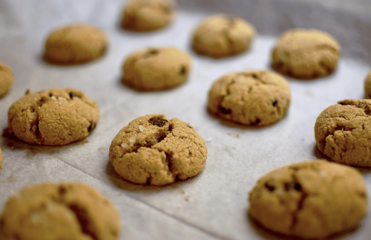 A dozen chickpea cookies that contain chocolate chips sit on a baking tray.