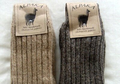 Two pairs of socks made from alpaca wool are folded and laying on a bed.